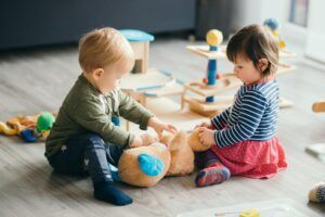 young boy and girl sitting on the floor playing with stuffed bear