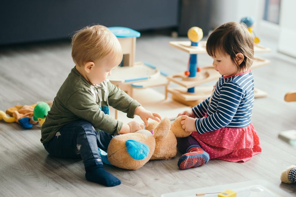 young boy and girl sitting on the floor playing with stuffed bear