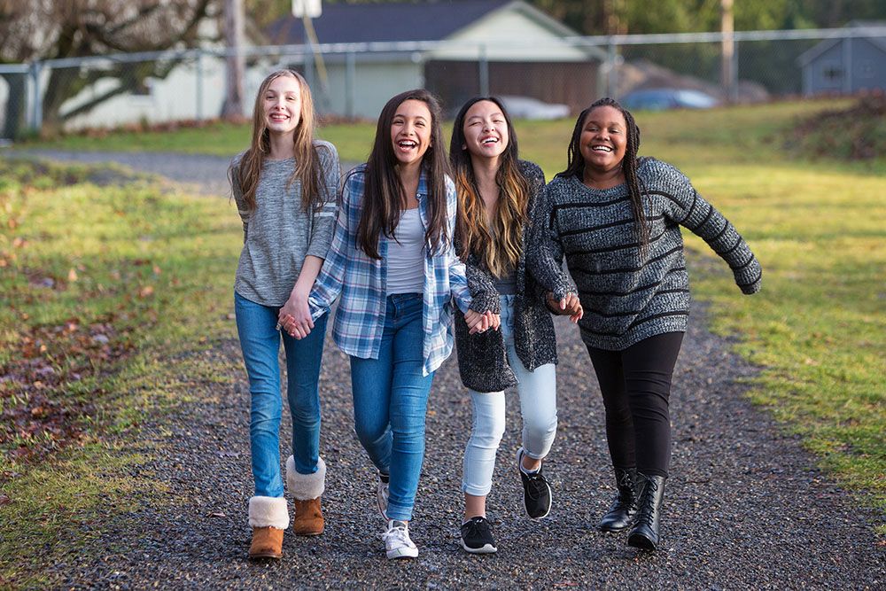four happy teenage girlfriends walking outdoors