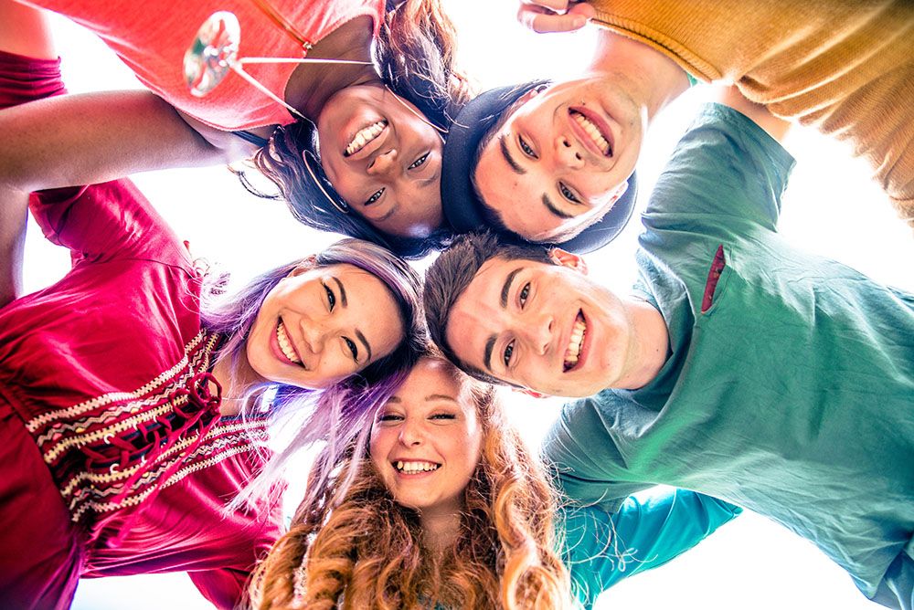 five teens in a circle looking down at the camera in the center